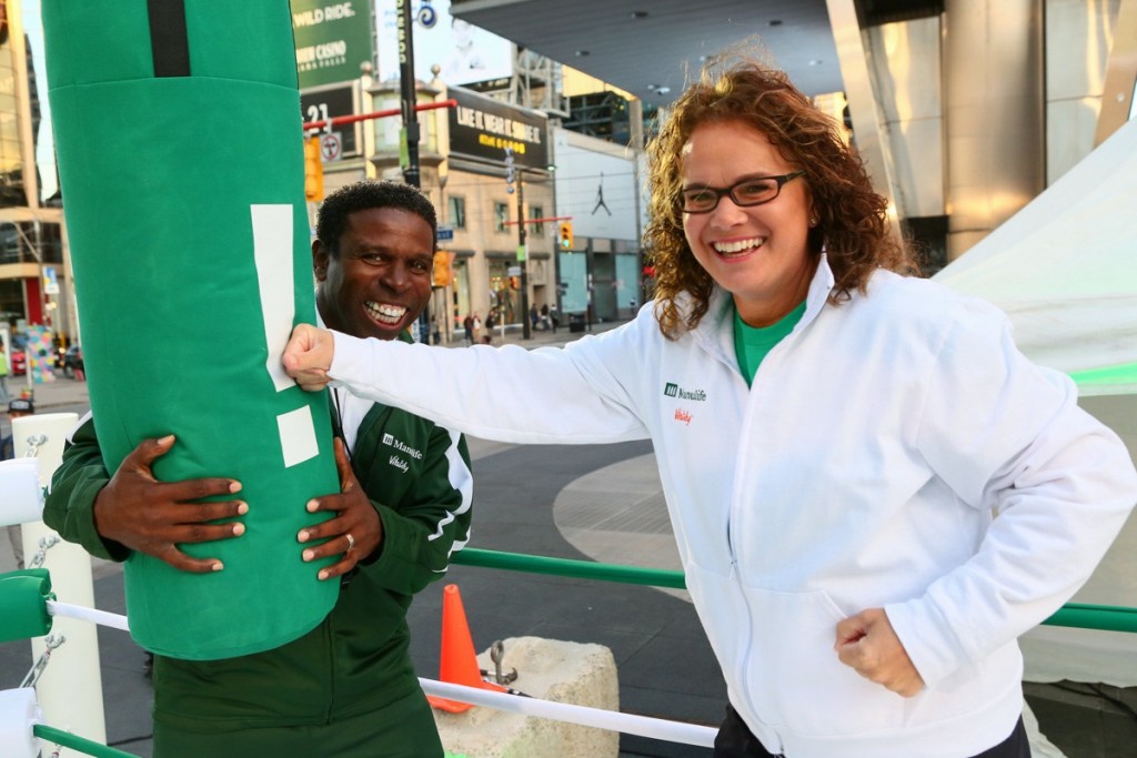 Manulife Canada President and CEO Marianne Harrison punches a message at the Manulife Vitality Workout Computer with Coach Michael Pinball Clemons in Toronto to launch Manulife Vitality, a new kind of life insurance that rewards healthy living. (CNW Group/Manulife Financial Corporation)